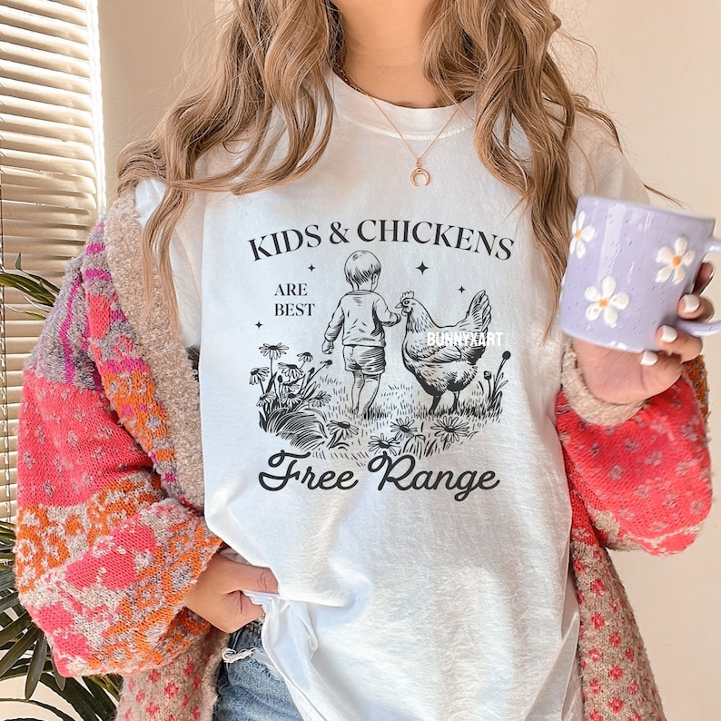 May include: White t-shirt with a black and white illustration of a child and a chicken. The text "Kids & Chickens Are Best Free Range" is printed on the shirt.