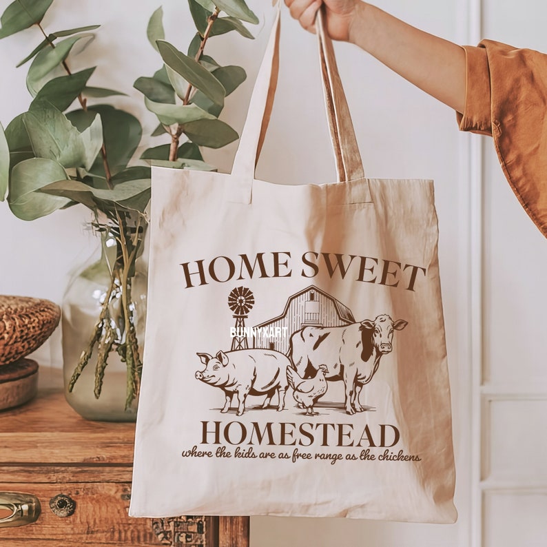 Pode incluir: Uma bolsa de lona branca com texto castanho que diz "Home Sweet Homestead, where the kids are as free range as the chickens". A bolsa apresenta uma ilustra&ccedil;&atilde;o castanha de um celeiro, uma vaca, um porco e uma galinha.