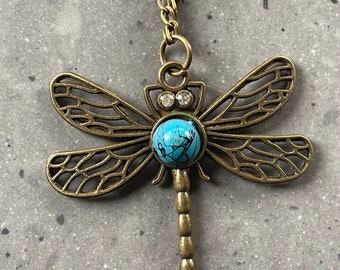 Pendentif libellule sur une chaîne en laiton avec une pierre turquoise.