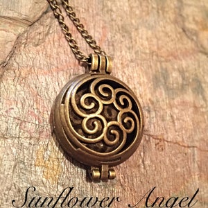 Può includere: Una collana dorata con un ciondolo rotondo che presenta un design decorativo a spirale. Il ciondolo è aperto e ha un coperchio incernierato.