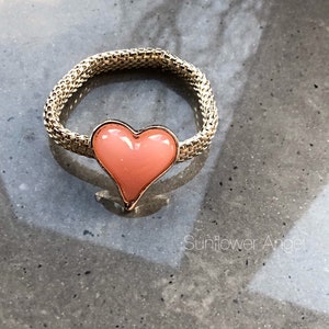 May include: A gold ring with a pink heart-shaped stone. The ring is made of a chain-like metal.