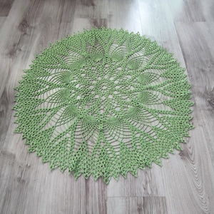 May include: A green crocheted doily with a delicate, intricate design. The doily is circular and has a scalloped edge.