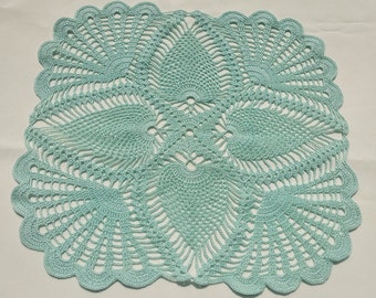 May include: A light blue, oval-shaped doily with a scalloped edge. The handmade doily features an intricate, openwork crochet design with a central floral motif and radiating fan-like patterns. The delicate texture and color create a vintage aesthetic.