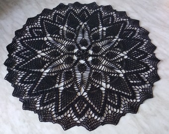 May include: A black crocheted doily with a delicate floral pattern. The doily is circular and has a scalloped edge.