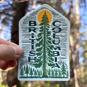 May include: A white sticker featuring a green pine tree at its centre. The tree is surrounded by smaller pine trees and a yellow sun. The words "BRITISH COLUMBIA" are written vertically on either side of the tree.