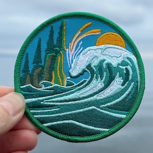 Peut inclure: Un patch brodé vert, bleu et blanc avec une vague qui se brise sur une île verte avec un soleil jaune en arrière-plan.
