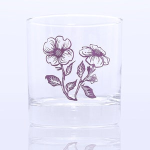 K&ouml;nnte beinhalten: Ein klares Glas mit einem violetten Blumenmuster. Die Blumen sind wei&szlig; mit violetten Umrissen und Stielen. Das Glas ist perfekt zum Servieren von Getr&auml;nken.