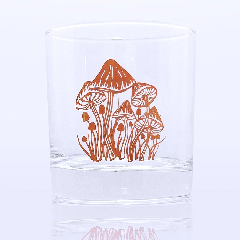 K&ouml;nnte beinhalten: Ein klares Glas mit einem Design aus orangefarbenen Pilzen, das auf die Seite gedruckt ist.