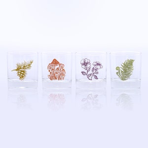 K&ouml;nnte beinhalten: Vier klare Glasbecher mit verschiedenen Naturmotiven. Die Becher zeigen eine Kiefernzapfen, Pilze, Blumen und einen Farn.
