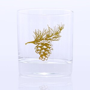 K&ouml;nnte beinhalten: Ein klares Glas mit einem goldenen Kiefernzapfen- und Zweigdesign.
