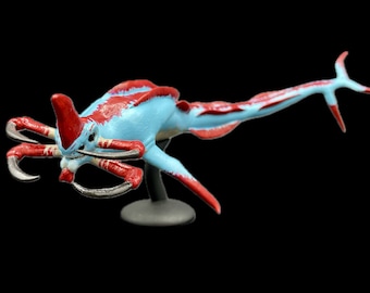 May include: A blue and red alien creature figurine with multiple legs and a long tail. The figurine is posed on a gray stand.