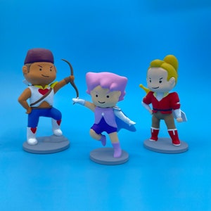 May include: Three hand-painted figurines of characters from a cartoon. The figurine on the left is a brown-skinned male character with a red heart on his chest, wearing a blue and red outfit. The figurine in the middle is a pink-skinned female character with a blue and purple outfit. The figurine on the right is a yellow-skinned male character with a red and yellow outfit.