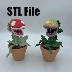以下が含まれることがあります： 口を開けて歯が見える、植物のような形をした3Dプリントされたフィギュアが2つあります。左側のフィギュアは、赤と白のキノコのような頭と緑の葉を持っています。右側のフィギュアは、緑と黄色の頭と緑の葉を持っています。両方のフィギュアは茶色の鉢に入っています。
