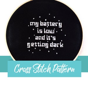 Pode incluir: Padrão de ponto cruz preto e branco em um aro de bordado redondo. O padrão diz "minha bateria está fraca e está escurecendo".