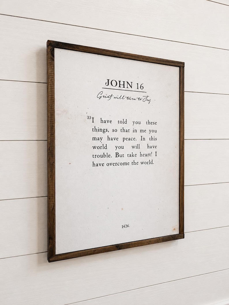 Puede incluir: Un marco de madera oscura que contiene una impresi&oacute;n con el texto "JOHN 16" y una cita sobre el dolor. El fondo es blanco con texto negro. El marco rectangular est&aacute; colgado en una pared blanca.