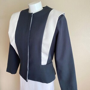 May include: A structured jacket featuring a dark charcoal gray base with contrasting white vertical panels running from the shoulders down to the waist. The garment has a round neckline, long sleeves, and a concealed front closure design.