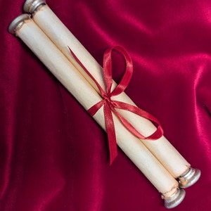 Puede incluir: Dos rollos enrollados atados con una cinta roja sobre un fondo de terciopelo rojo.