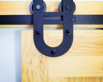 May include: Black metal U-shaped sliding barn door hardware with two black rollers and a wooden door.