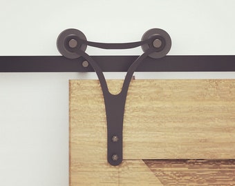 May include: Black metal sliding door hardware with two rollers and a decorative Y-shaped bracket. The hardware is mounted to a wooden door.
