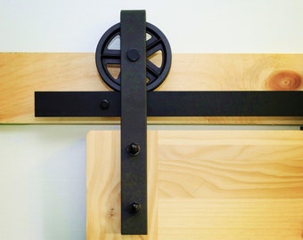 May include: Black metal sliding barn door hardware with a round wheel and a black track. The hardware is mounted on a light wood door.