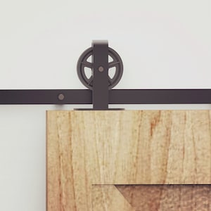 May include: A black metal sliding door track with a single black metal roller. The track is mounted to a light wood door.