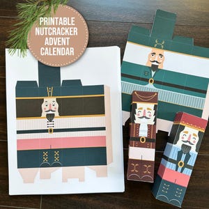 May include: Printable Nutcracker Advent Calendar with various nutcracker designs in green, brown, and pink. The image includes assembled and unassembled paper cutouts, with text that reads "Printable Nutcracker Advent Calendar."