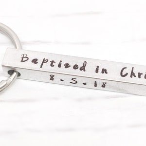 May include: Silver keychain with a rectangular bar engraved with the text "Baptized in Christ 8-5-18".
