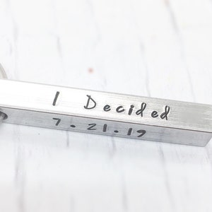 May include: Silver key chain with a rectangular bar that reads "I Decided 7.21.19".