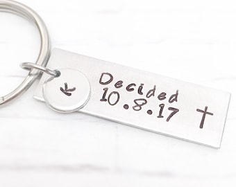 May include: Silver keyring with a small charm featuring the letter "K" and a rectangular tag inscribed with "Decided 10.8.17" and a cross.