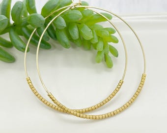 May include: Gold hoop earrings with a beaded detail. The beads are a light beige color.