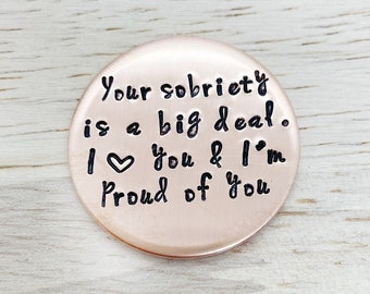 Peut inclure: Un jeton rond de couleur cuivre avec le texte "Your sobriety is a big deal. I ♥ you & I'm proud of you" gravé en noir.