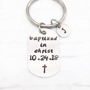 May include: Silver keychain with a silver tag that reads "baptized in christ 10.24.18" with a small cross below the date. A small silver charm with the letter "J" is attached to the keychain.