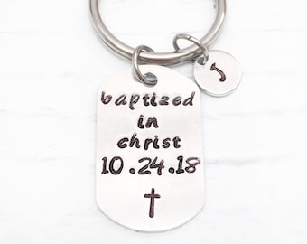 May include: Silver keyring with a silver tag that reads "baptized in christ 10.24.18" with a small cross below the date. A small silver charm with the letter "J" is attached to the keyring.