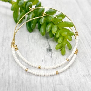 May include: Gold hoop earrings with two rows of white beads.