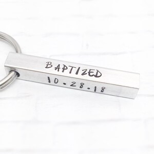 May include: Silver key chain with a rectangular bar engraved with the words "BAPTIZED 10-28-18".