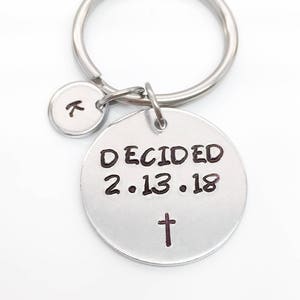 May include: Silver keychain with a round charm that says "DECIDED 2.13.18" with a cross below the date. A smaller charm with the letter "K" is attached to the keychain.