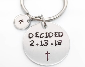 May include: Silver keyring with a round charm that says "DECIDED 2.13.18" with a cross below the date. A smaller charm with the letter "K" is attached to the keyring.
