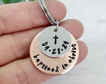 May include: A silver and copper keychain with a cross and the text "Dt. 28.24 baptized in christ".