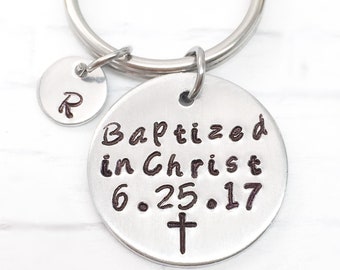 May include: A silver keyring with two circular pendants. The larger pendant has the words "Baptized in Christ 6.25.17" and a cross. The smaller pendant has the letter "R".