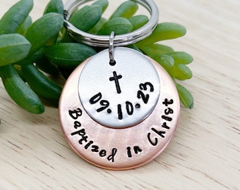May include: A silver and copper keychain with the words "Baptized in Christ" and a cross with the date "09.10.23".