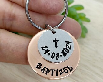 May include: A silver and copper keyring with a cross and the date "24.08.2024" on one side and the word "BAPTIZED" on the other side.