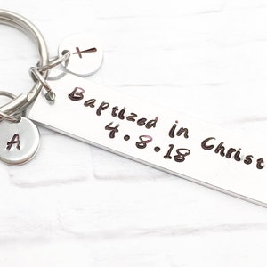 May include: Silver keychain with a rectangular tag that reads "Baptized in Christ 4.8.18". The keychain also has a small charm with the letter "A" and another charm with a cross.
