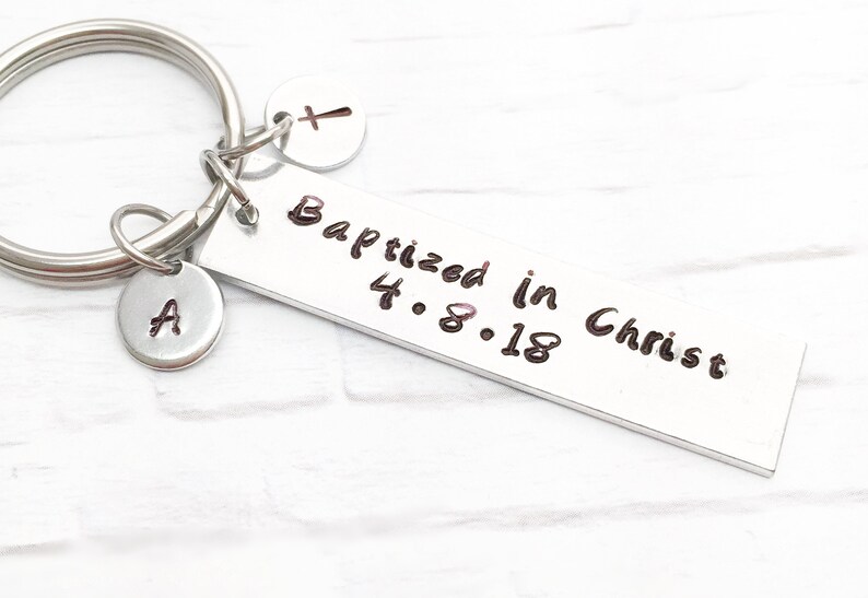 May include: Silver keychain with a rectangular tag that reads "Baptized in Christ 4.8.18". The keychain also has a small charm with the letter "A" and another charm with a cross.