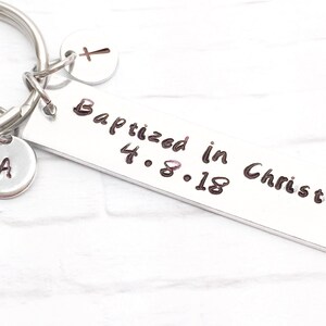 May include: Silver keychain with a rectangular tag that reads "Baptized in Christ 4.8.18". The keychain also has a small charm with a cross and another charm with the letter "A".