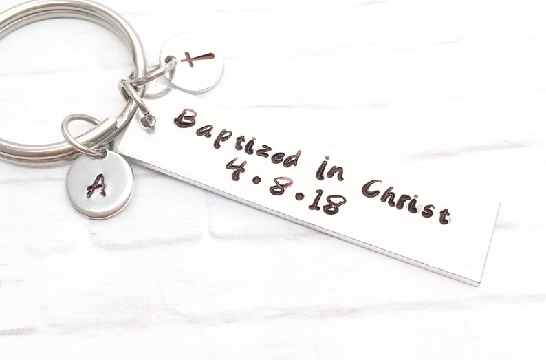 May include: Silver keychain with a rectangular tag that reads "Baptized in Christ 4.8.18". The keychain also has a small charm with a cross and another charm with the letter "A".