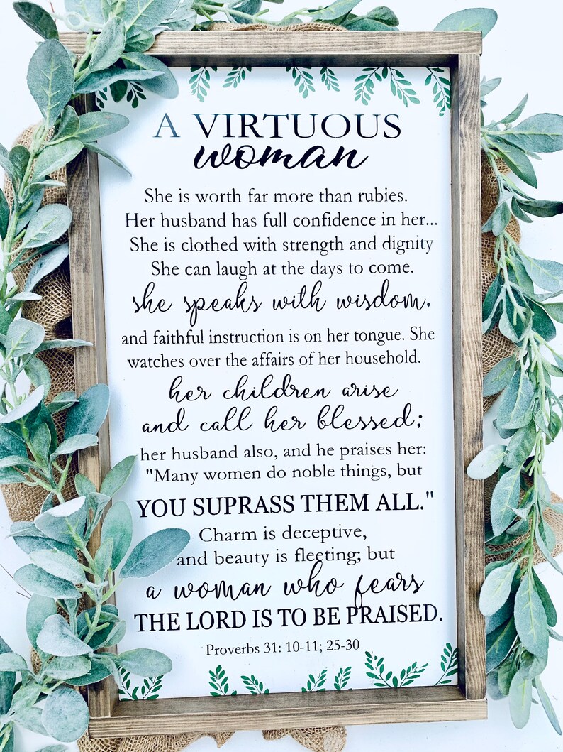 May include: A rectangular wooden sign with a dark brown frame featuring the text A VIRTUOUS WOMAN and verses from Proverbs 31: 10-11; 25-30 printed in black on a white background, accented with green leaf illustrations at the top and bottom.