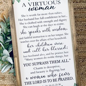 May include: A rectangular wooden framed sign with a white background featuring green leaf illustrations at the top and bottom. The text reads A VIRTUOUS woman, She is worth far more than rubies, Her husband has full confidence in her, She is clothed with strength and dignity, She can laugh at the days to come, she speaks with wisdom, and faithful instruction is on her tongue, She watches over the affairs of her household, her children arise and call her blessed, her husband also, and he praises her, MANY WOMEN DO NOBLE THINGS, BUT YOU SUPRASS THEM ALL, Charm is deceptive, and beauty is fleeting, but a woman who fears THE LORD IS TO BE PRAISED, Proverbs 31: 10-11; 25-30.