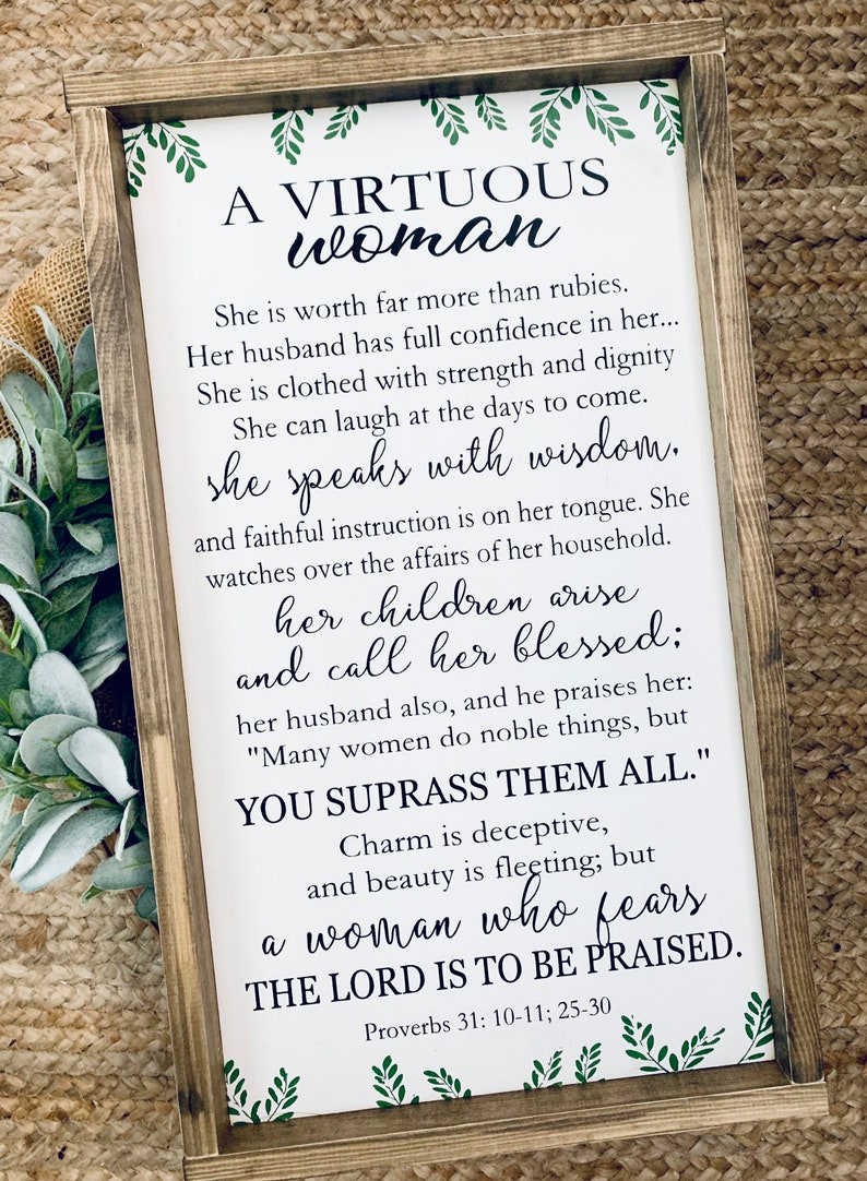 May include: A rectangular wooden framed sign with a white background featuring green leaf illustrations at the top and bottom. The text reads A VIRTUOUS woman, She is worth far more than rubies, Her husband has full confidence in her, She is clothed with strength and dignity, She can laugh at the days to come, she speaks with wisdom, and faithful instruction is on her tongue, She watches over the affairs of her household, her children arise and call her blessed, her husband also, and he praises her, MANY WOMEN DO NOBLE THINGS, BUT YOU SUPRASS THEM ALL, Charm is deceptive, and beauty is fleeting, but a woman who fears THE LORD IS TO BE PRAISED, Proverbs 31: 10-11; 25-30.
