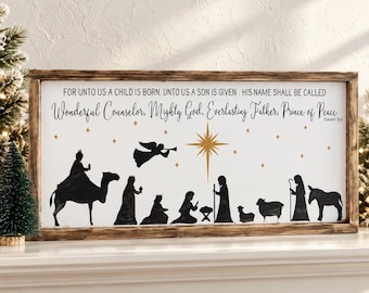 May include: A rectangular wooden-framed sign with a white background featuring a black silhouette of a nativity scene. The text reads: FOR UNTO US A CHILD IS BORN. UNTO US A SON IS GIVEN. HIS NAME SHALL BE CALLED Wonderful Counselor, Mighty God, Everlasting Father, Prince of Peace. ISAIAH 9:6. A gold star and small gold stars are above the figures.