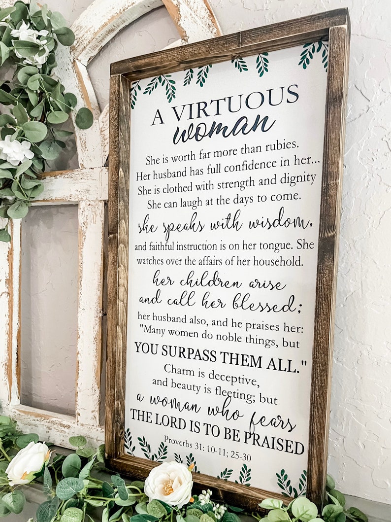 May include: A rectangular wooden sign with a dark brown frame and a white background featuring black text from Proverbs 31: 10-11; 25-30. The sign includes green leaf illustrations at the top and bottom borders, displaying the title A VIRTUOUS woman.